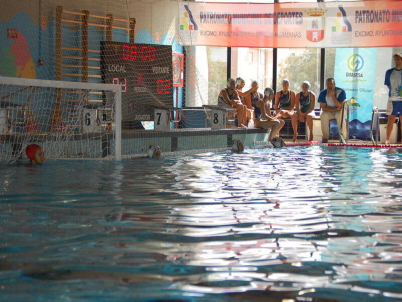 Jugadores de waterpolo en acción durante un partido en una piscina cubierta.