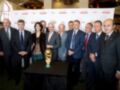 Un grupo de hombres en trajes posa junto a una copa del Mundial de fútbol, en un evento organizado por Cruzcampo.