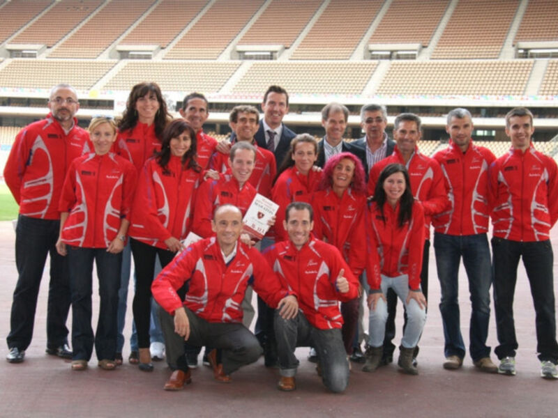 Equipo deportivo en un estadio, todos vestidos con chaquetas rojas y blancas, sonrientes y celebrando juntos.