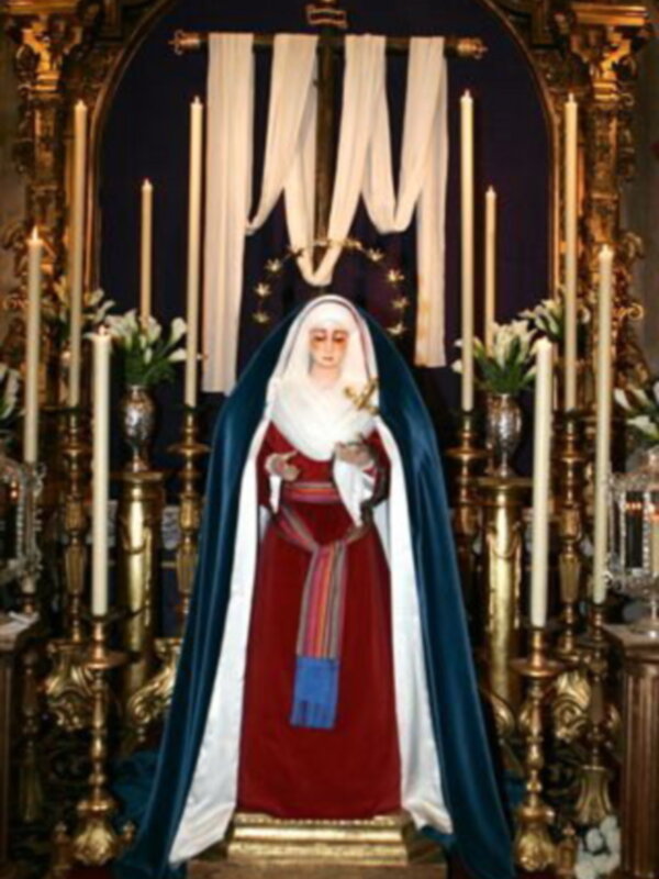 Estatua de la Virgen María en un altar con velas y flores, rodeada de una decoración religiosa.