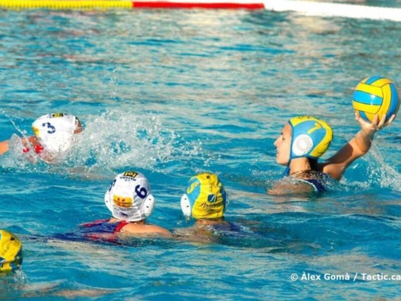 Jugadores de waterpolo en acción durante un partido, con balones y uniformes visibles en una piscina.