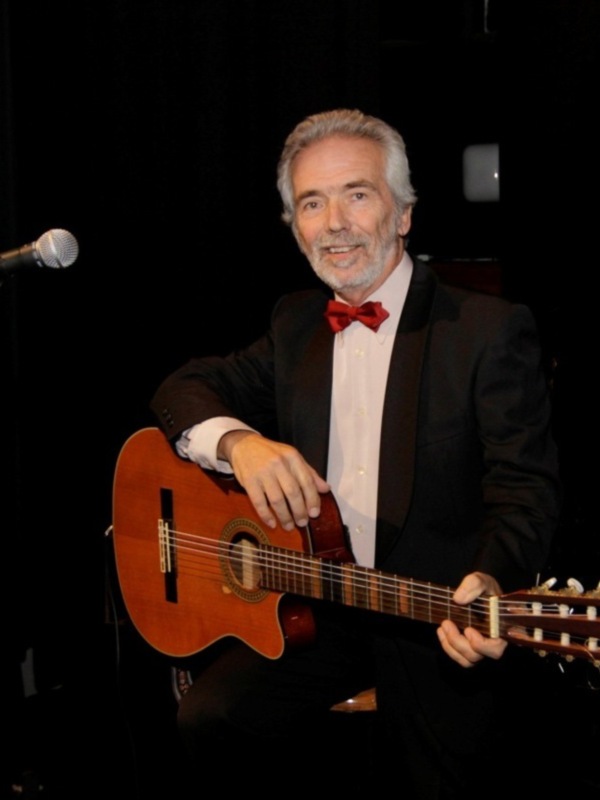 Artista tocando la guitarra clásica en un escenario con microfono.