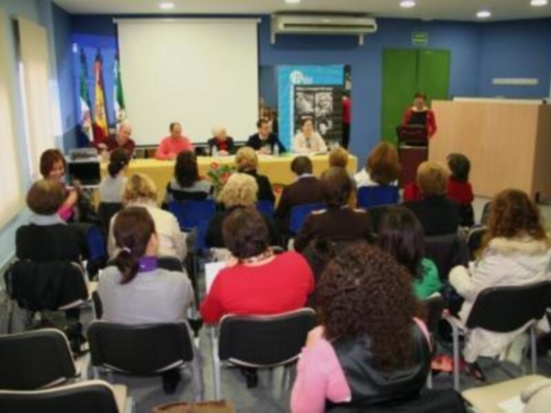 Una conferencia en un aula con personas sentadas en sillas y un panel de presentación en el fondo.