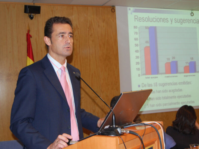 Hombre hablando en un evento de presentación con un gráfico de resoluciones y sugerencias en la pantalla.