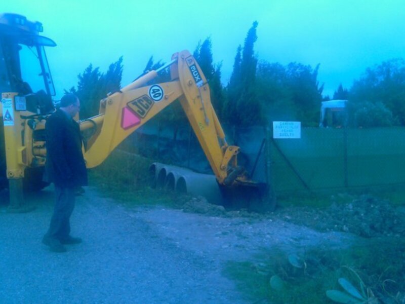 Operario supervisando la excavación de tuberías con una excavadora JCB en un entorno residencial.