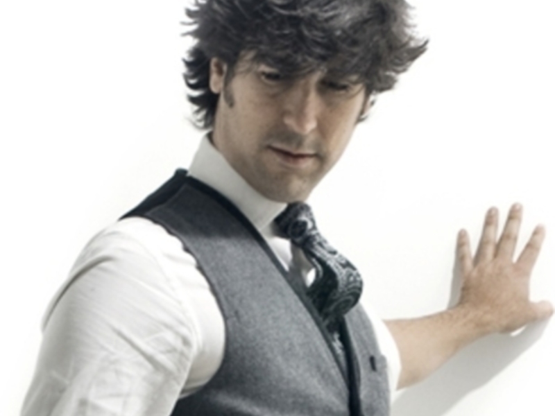 Elegante hombre con chaleco y corbata, apoyado en una pared blanca.