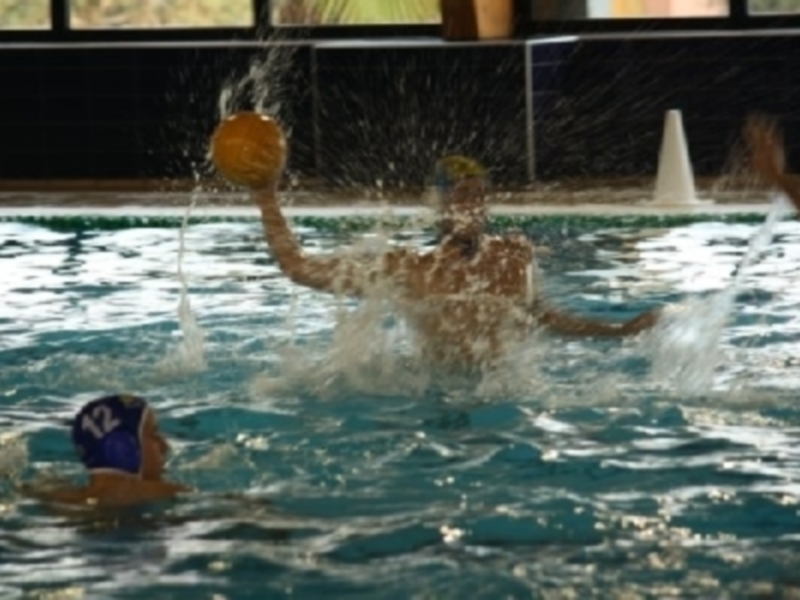 Jugadores de waterpolo en acción, lanzando el balón en un partido en piscina.