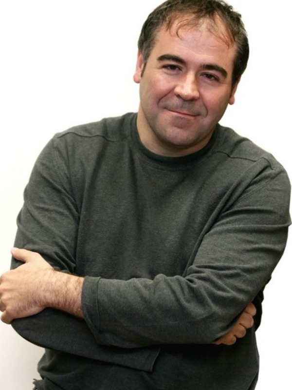 Persona con camisa negra y brazos cruzados, sonriendo ligeramente.
