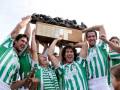Equipo de fútbol celebrando su victoria con un trofeo y una caja, todos vestidos con camisetas verdes y blancas.