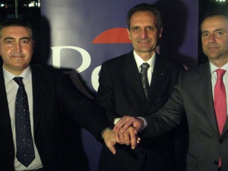 Tres hombres en trajes de negocios posan juntos, aparentemente en una conferencia o evento profesional.