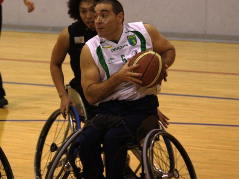 Un jugador de baloncesto en silla de ruedas controla el balón durante un partido en un gimnasio.