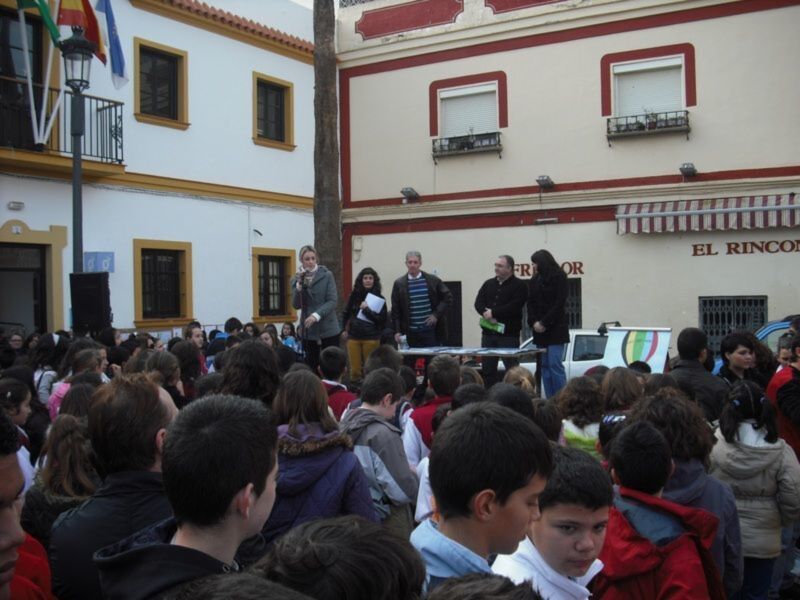 Celebración en la plaza frente a 'El Rincon' con un grupo de personas reunidas, posiblemente para una actividad o evento público.