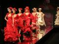 Una escena de moda flamenca con modelos vestidos de rojo brillante y complementos florales, posando en una pasarela.