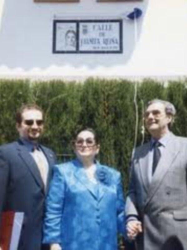 Tres personas posando juntas frente a una placa conmemorativa de la calle Juanita Rivas.