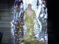 Modela en la pasarela con un vestido dorado brillante, proyectado con luces multicolores en la noche.