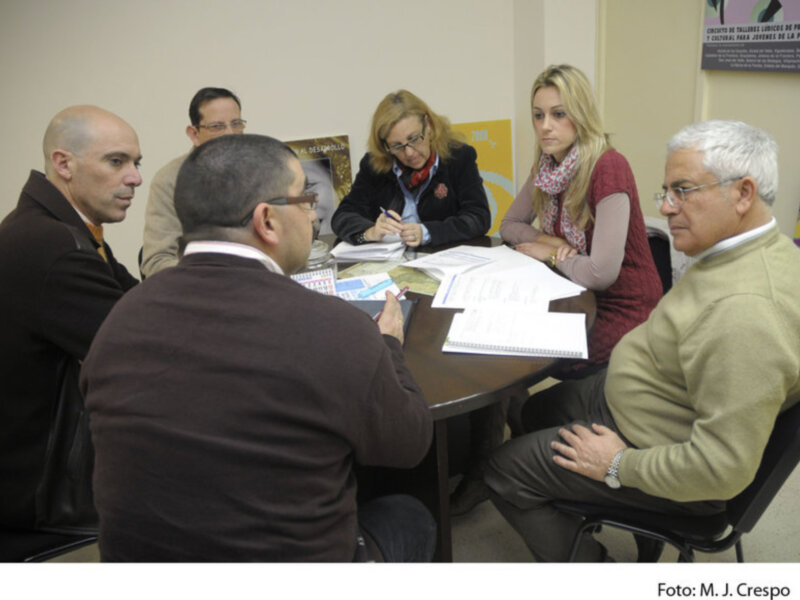 Reunión de trabajo en una oficina, participantes discutiendo y revisando documentos.