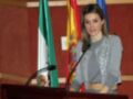 Mujer hablando en un podium con banderas de España y Andalucía en el fondo.