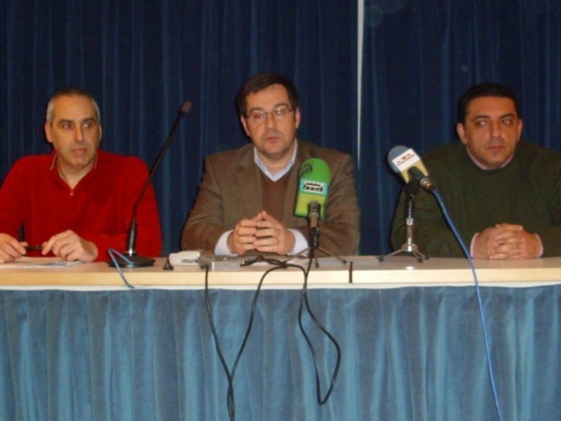 Tres personas sentadas en una mesa con micrófonos, probablemente en una conferencia o reunión.