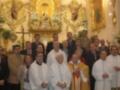 Una imagen festiva de una iglesia llena de altares dorados y flores, con varios sacerdotes vestidos en diferentes estilos de vestimenta religiosa.