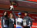 Triunfantes en el podio de una carrera ciclista, con una mujer en el centro sosteniendo un trofeo y una mujer a su lado sonriendo, frente a un cartel con el nombre 'Cruzcampo'.