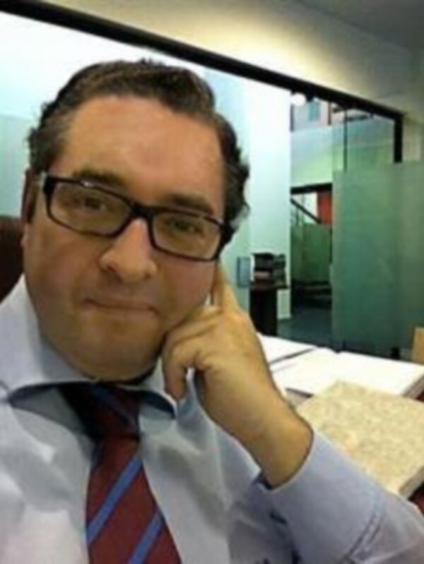 Un hombre con gafas y corbata en un entorno de oficina, apoyado en la mano con un gesto pensativo.