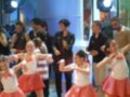 Niñas bailando en un programa de televisión con adultos detrás.