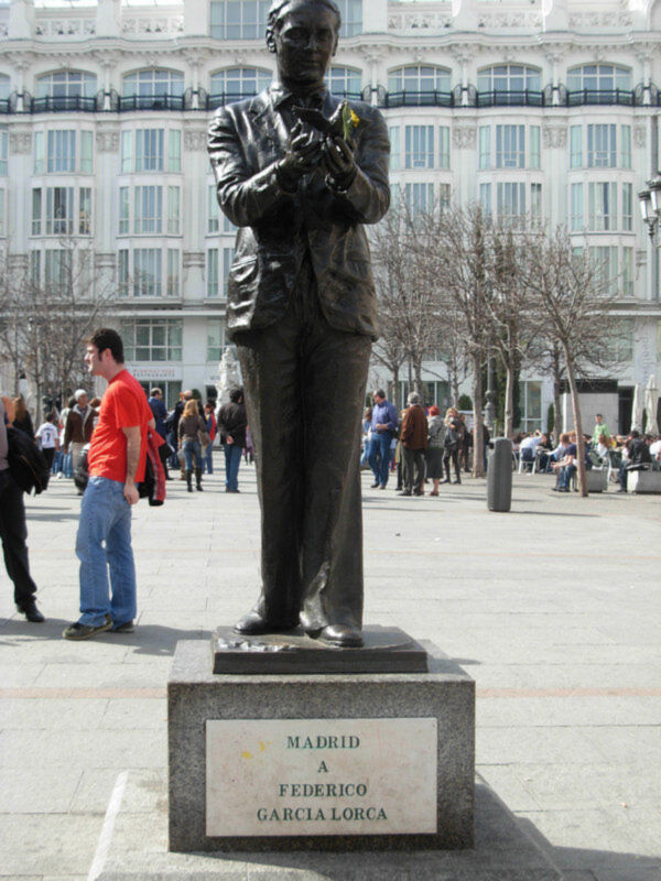 Estatua de Federico García Lorca en Madrid, España, con personas visitando el monumento en un día soleado.