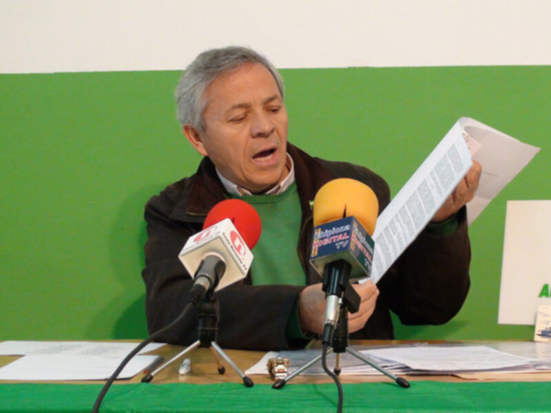 Persona hablando en rueda de prensa del Partido Andalucista, con micrófonos y documentos en la mesa.
