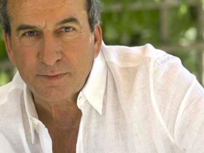 Un hombre con una camisa blanca y una expresión seria, posiblemente en un entorno natural.