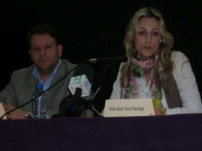 Conferencia de prensa con dos participantes sentados detrás de un panel con micrófonos y firmas de identificación.