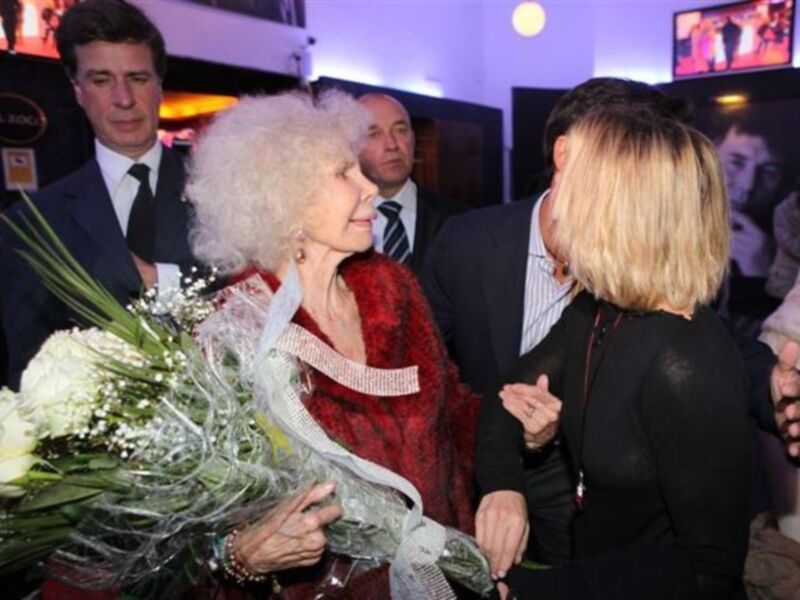 Celebración de una celebridad con un ramo de flores en un evento formal.