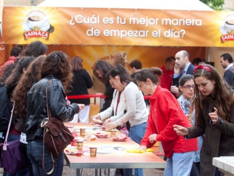 Una multitud de personas disfrutando de una comida al aire libre, con una banderola que pregunta: '¿Cuál es tu mejor manera de empezar el día?'