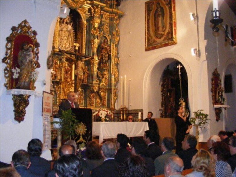 Celebración religiosa en una iglesia con altares dorados y un altar con velas y flores.
