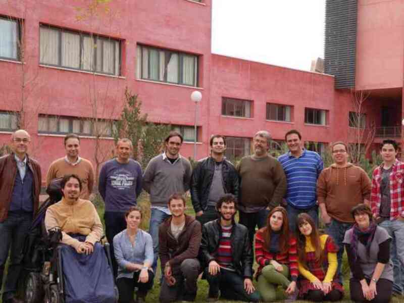 Grupo de personas posando al aire libre frente a un edificio rojo.