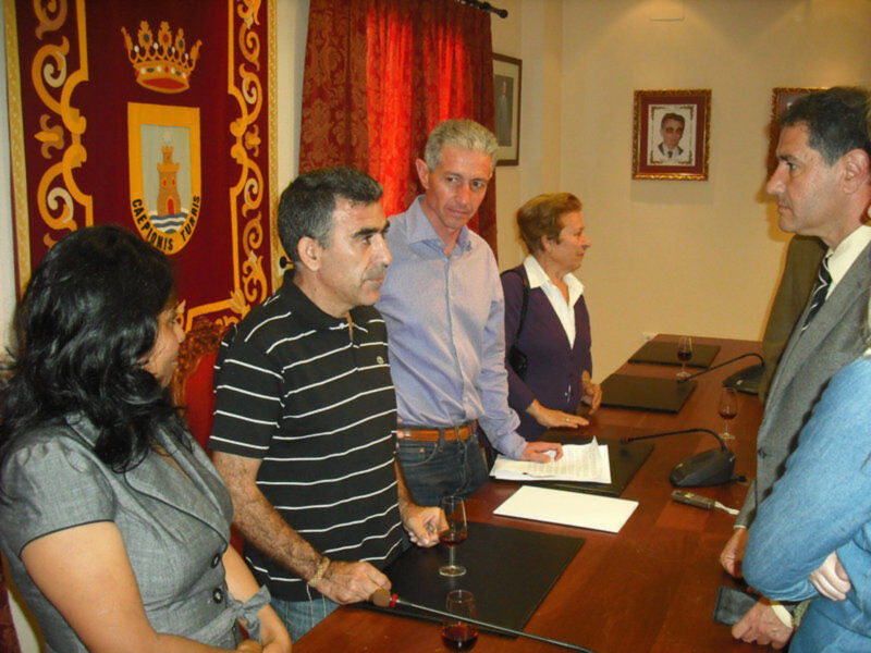Reunión en un salón de actos con personas discutiendo sobre documentos y bebidas.