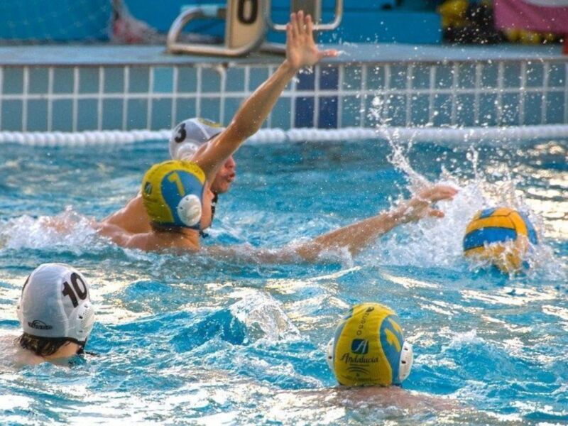 Jugadores de waterpolo en acción, uno lanza el balón mientras otro se prepara para interceptarlo en un partido intenso.