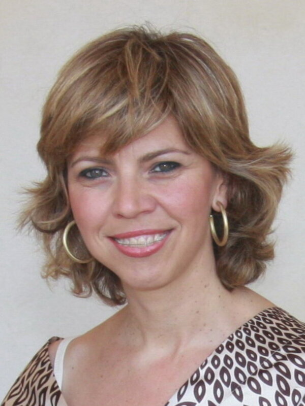 Retrato de mujer con cabello corto ondulado y orejeras doradas, sonriendo con expresión amistosa.