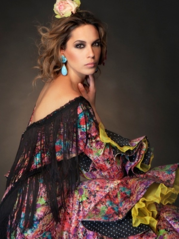 Retrato de mujer en vestido flamenca con flores y flecos, expresión serena.