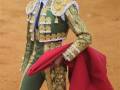 Un torero en traje tradicional sostiene un capote rojo mientras prepara para una corrida de toros en la plaza de toros.