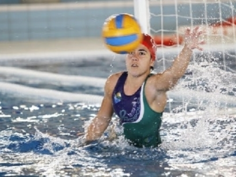 Jugadora de waterpolo en acción, lanzando el balón hacia la portería.