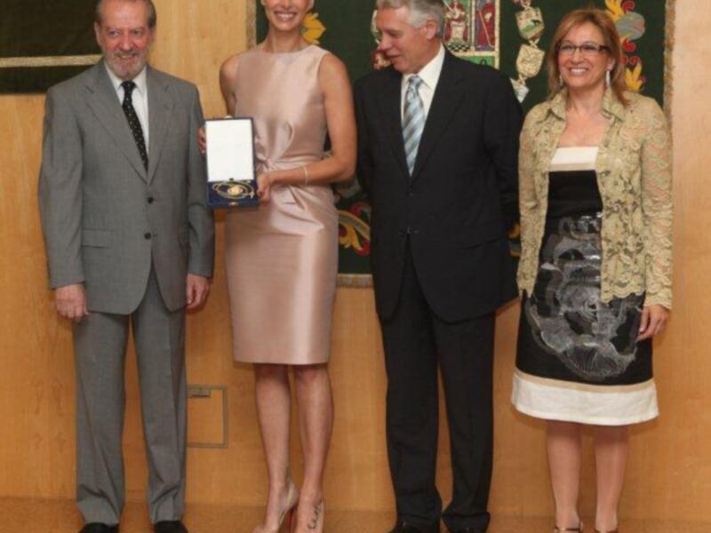 Premio entregado en una ceremonia formal, con una mujer recibiendo un reconocimiento de manos de autoridades.