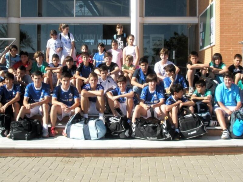 Un grupo de jóvenes jugadores de fútbol posando frente a una entrada de edificio, con sus maletas a los pies, listos para un viaje o un entrenamiento.