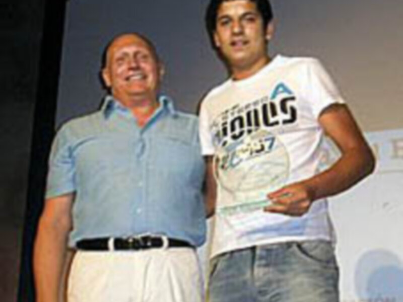 Dos hombres posando juntos, uno con camiseta blanca y el otro con camiseta azul, en un evento público.