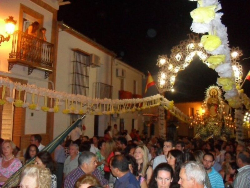 Procesión nocturna con imagen religiosa en España, rodeada de espectadores en una calle iluminada.