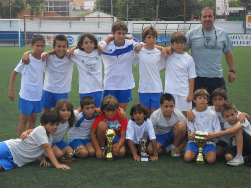 Equipo de fútbol infantil celebrando con trofeos en un campo de fútbol.