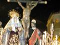 Imagen de una procesión religiosa nocturna con figuras de Jesús en la cruz y María, rodeadas por velas y flores.