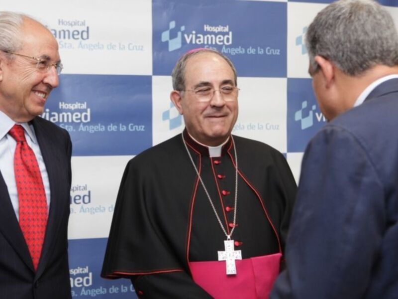 Un hombre en traje y otro en hábito sacerdotal sonríen durante una reunión en el Hospital Viamed Santa Ángela de la Cruz.