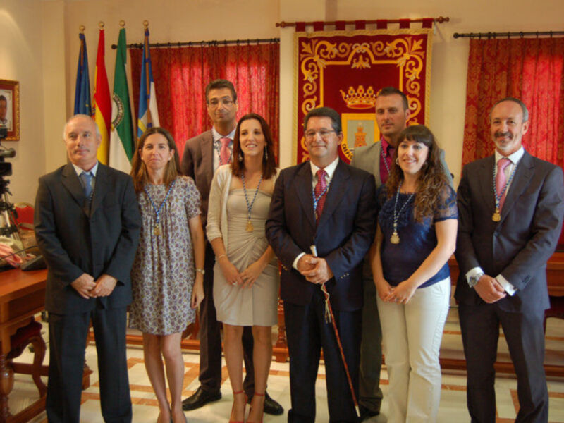 Grupo de personas posando para una foto en un entorno formal con banderas y un escudo en el fondo.
