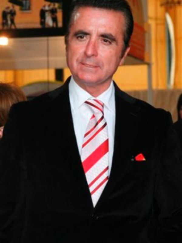 Hombre vestido con traje negro y corbata roja con rayas blancas, posando para la cámara.
