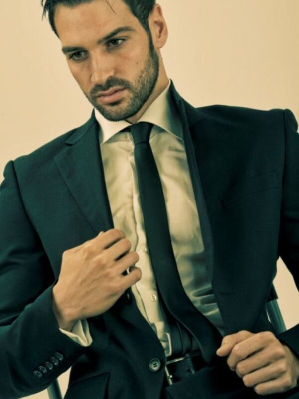 Elegante hombre en traje oscuro ajustando su corbata, con un fondo neutro y un tono cálido.